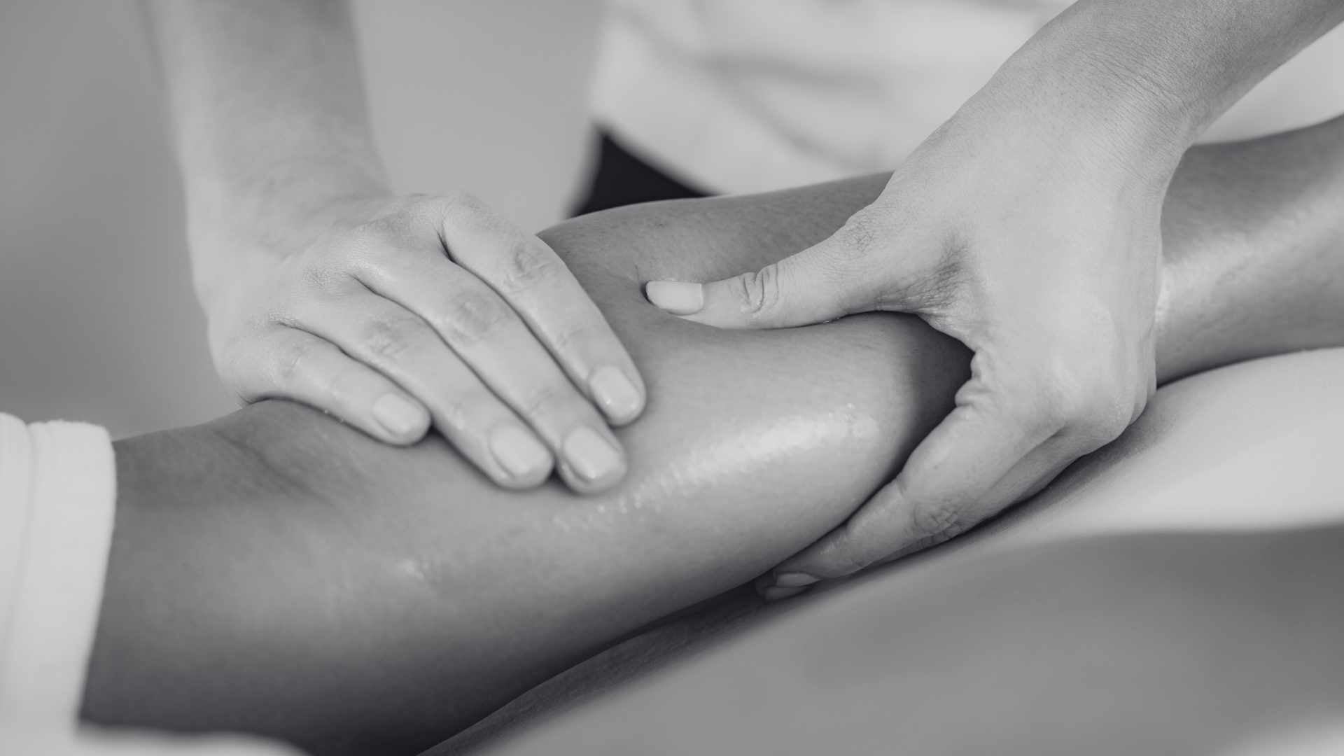 Therapist performing a sports massage on a client's leg in black and white.