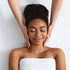 A birds eye view of a lady lying down on a towel smiling whilst a therapist has both hands either side of her face.