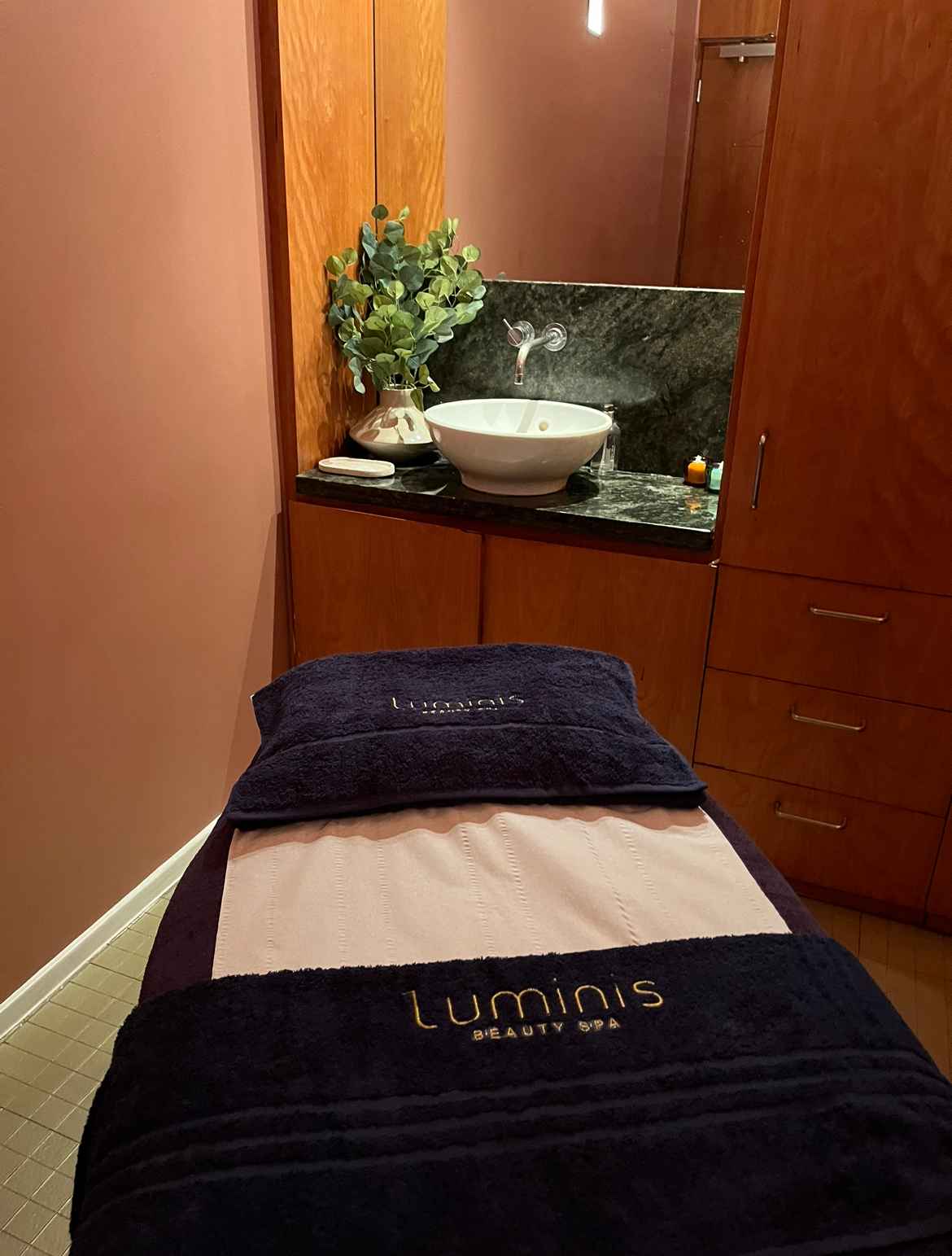 A modern massage bed in a Luminis Canary Wharf treatment room with Luminis branded towels. 