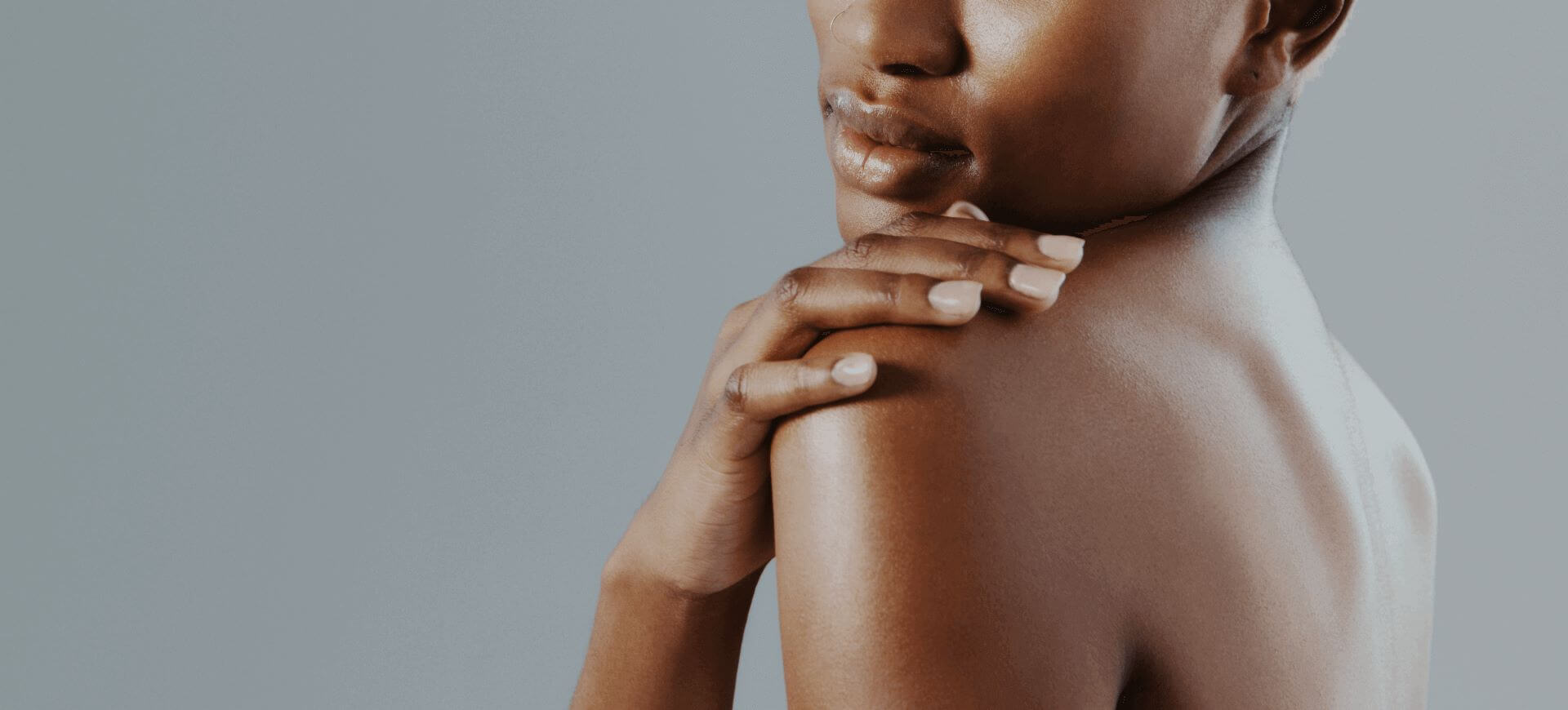 A landscape close up of a woman's back and shoulder featuring freshly manicured nails on her hand that is holding onto the shoulder.