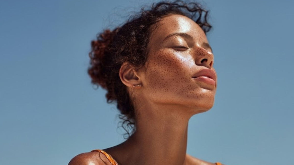 A woman with glowy skin and eyes closed against a blue sky background