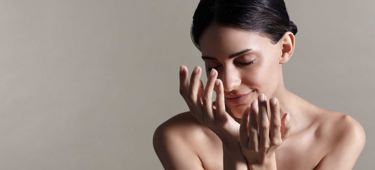 A woman with her hands contorted and eyes closed against a grey background