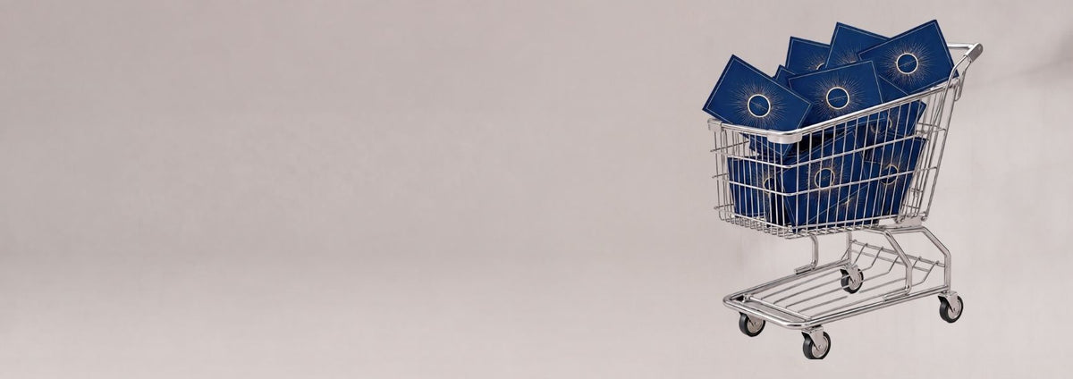 A silver metal shopping cart holding several blue rectangular boxes with circular cutouts, photographed on a plain light gray studio background with open space on the left.