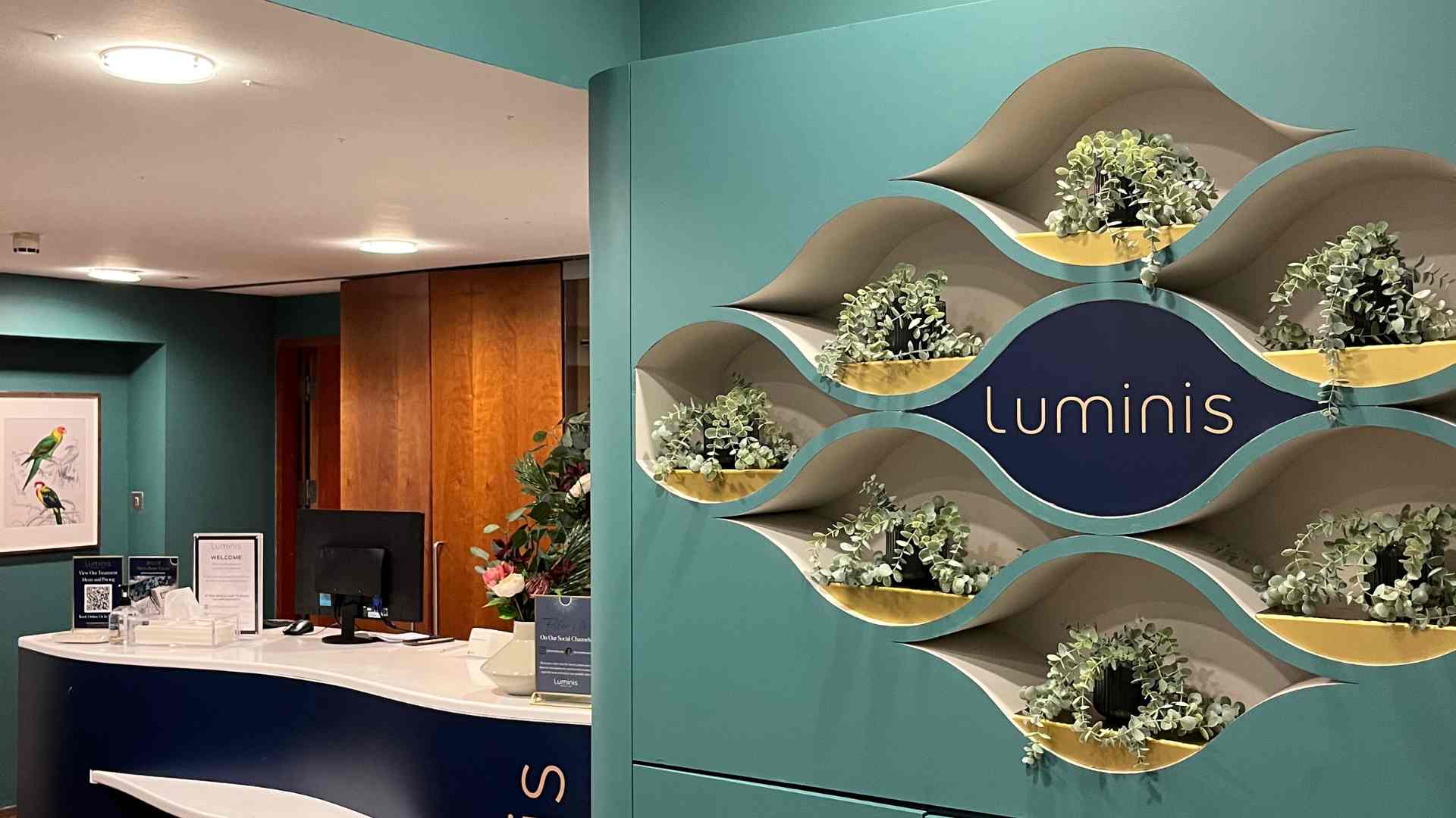 The reception of a Luminis Beauty Spa in Canary Wharf with tones of blue colours, and plants in cut-outs on the wall. 