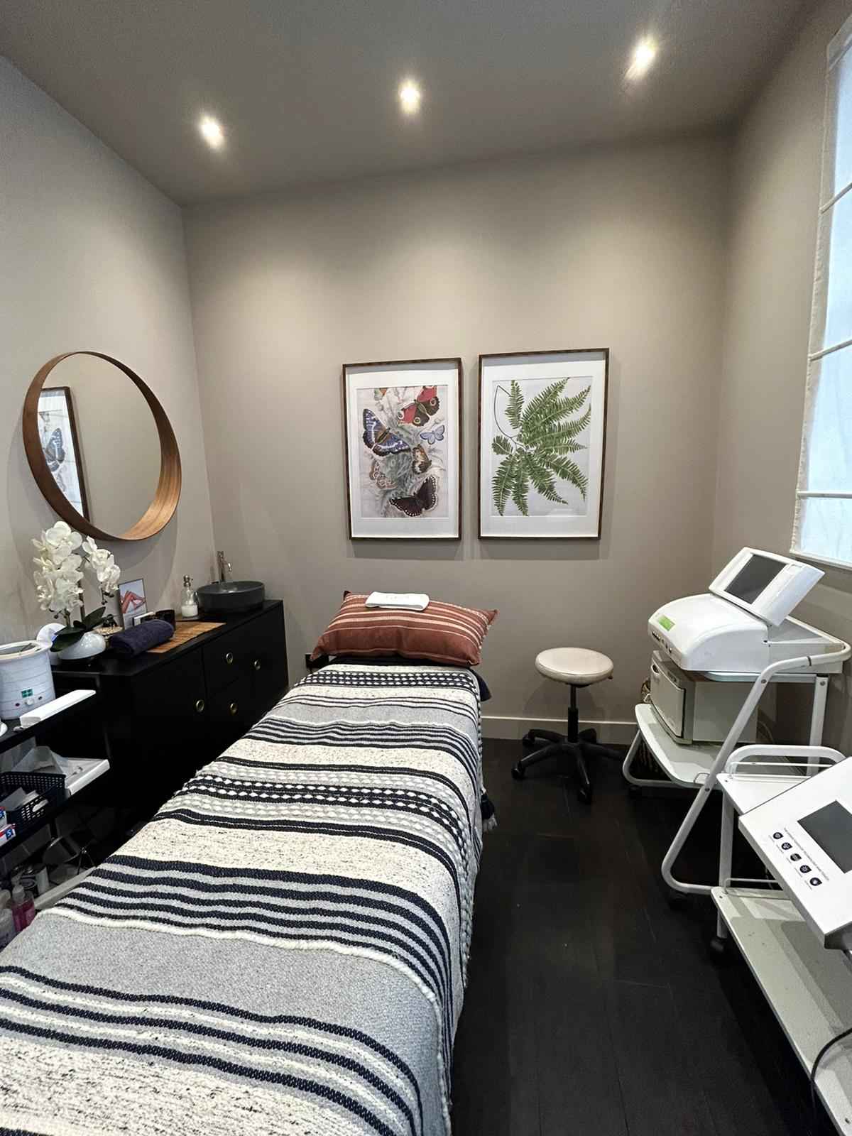  A modern beauty treatment room with patterned boho towelling on massage bed, featuring two jungle inspired prints on the wall behind. 