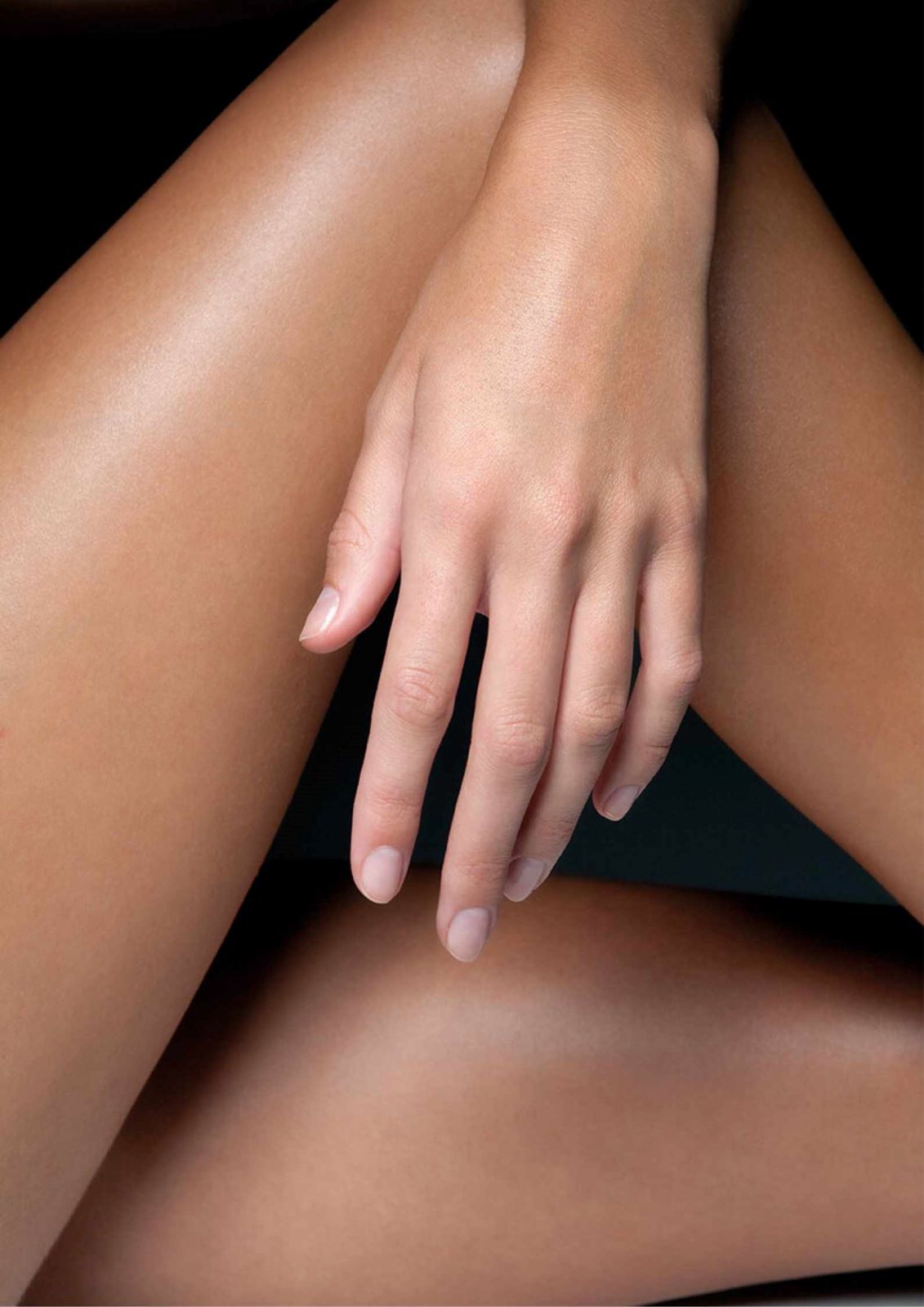 A close up of a woman's smooth legs crossed over with her hand resting on her knee. 