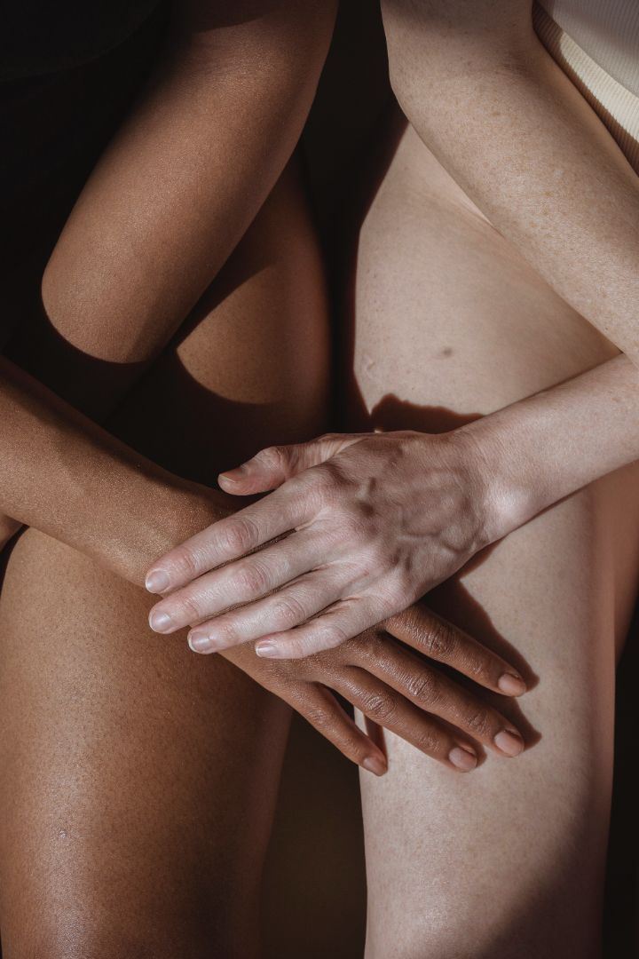 A close up of two woman with smooth skin sitting side by side with their hands on each others legs. 