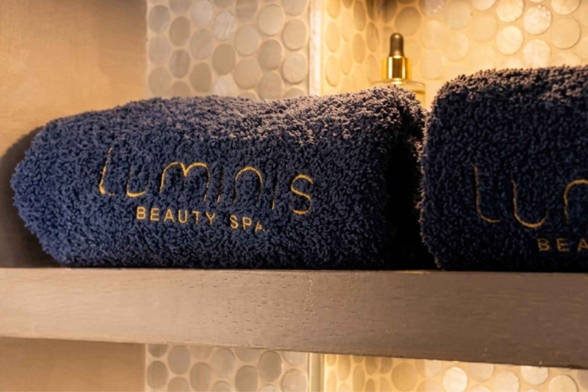 Two blue towels with 'Luminis Beauty Spa' branding on a shelf.