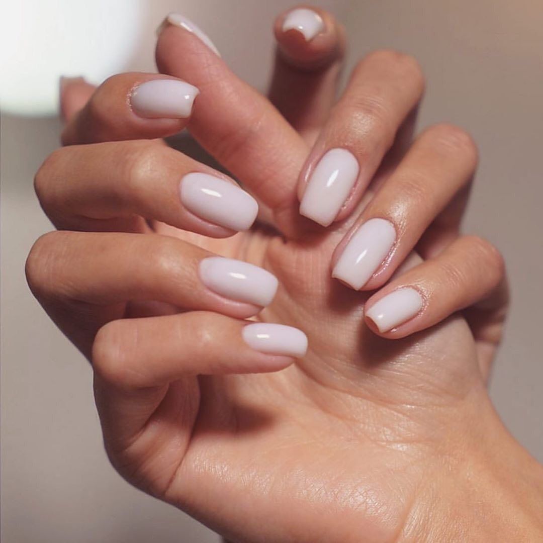A close up of a woman displaying her freshly gel manicured nails, featuring a baby pink nail polish colour.