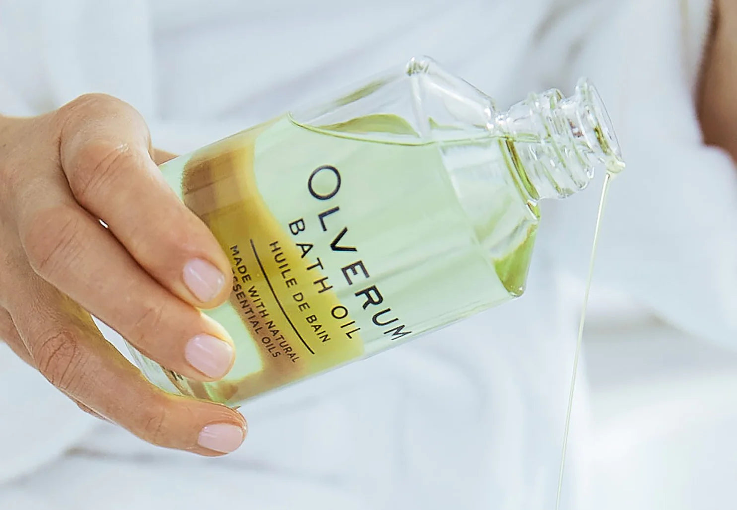 A close up of a person pouring Olverum Bath Oil. 