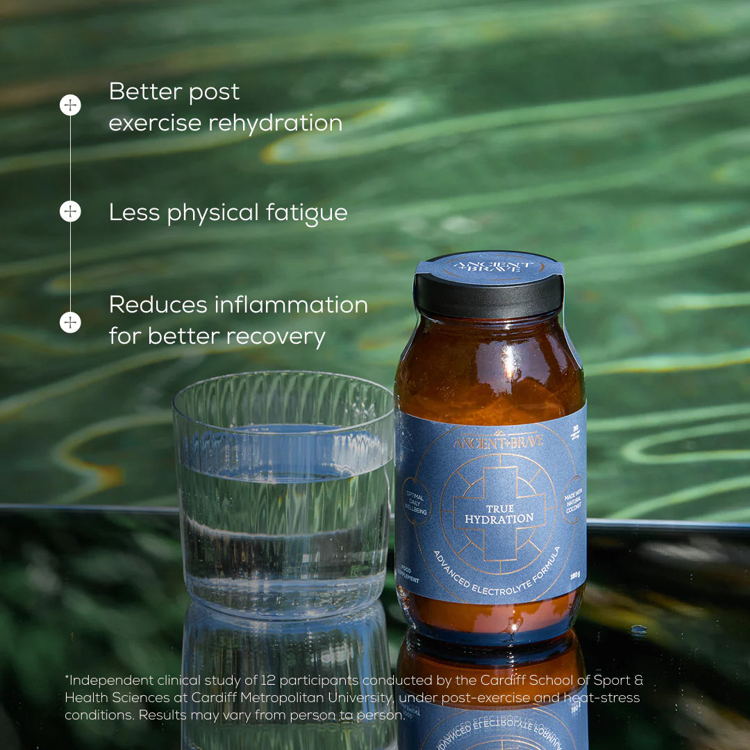 Bottle of True Hydration supplement with a glass of water on a reflective surface with greenery in the background.