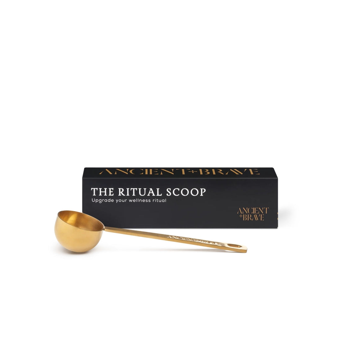 A gold-colored brass ritual scoop with a long handle lies in front of its black packaging box, which features gold lettering that reads &