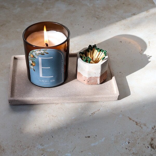 A product shot of Luminis owned Esperance candle whilst lit and accompanied by matches on a tray with a marbled background. 