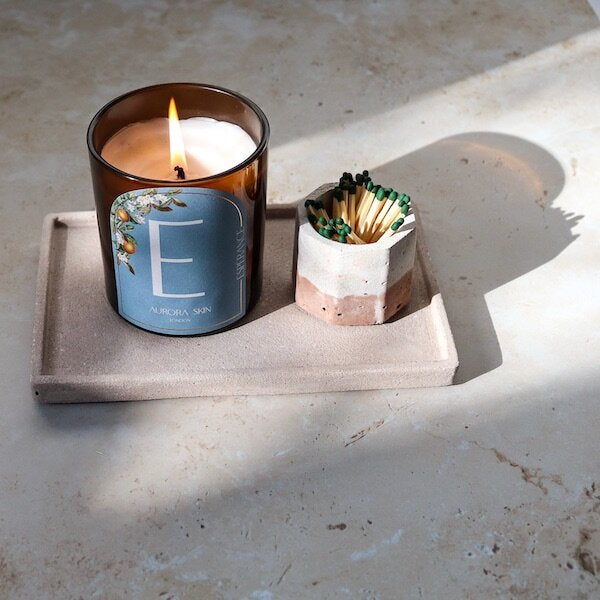 A product shot of Luminis owned Esperance candle whilst lit and accompanied by matches on a tray with a marbled background.